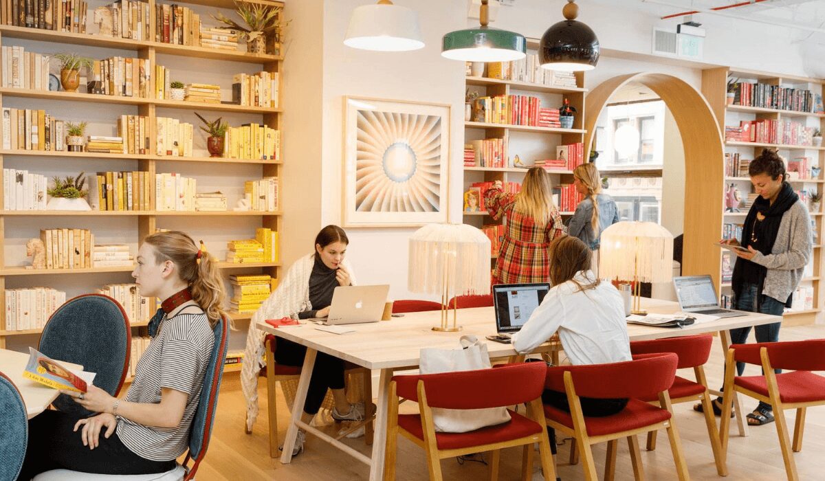 People working and socializing in a cozy, well-lit cafe with bookshelves.